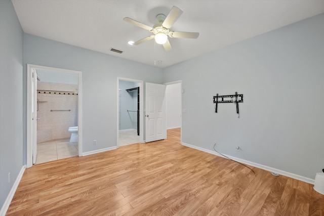 unfurnished bedroom featuring a walk in closet, connected bathroom, light hardwood / wood-style floors, and ceiling fan