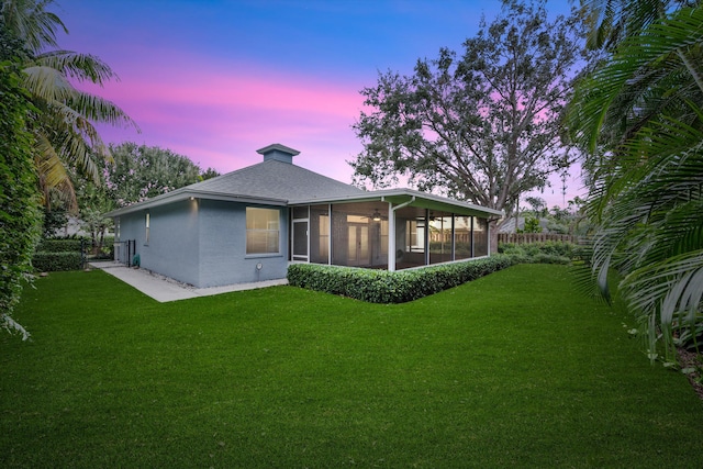 back house at dusk featuring a sunroom and a lawn