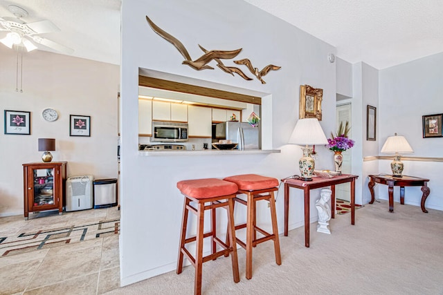 kitchen with kitchen peninsula, appliances with stainless steel finishes, light colored carpet, ceiling fan, and white cabinets