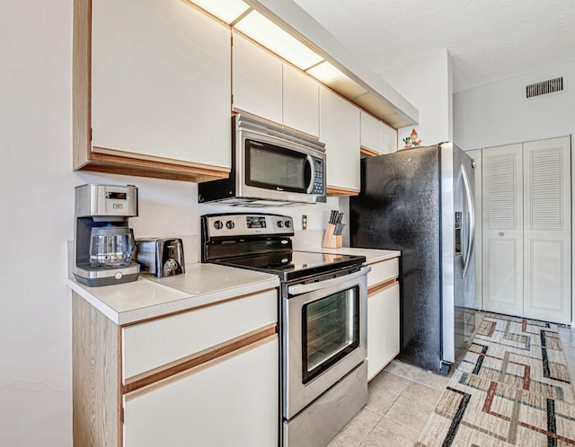 kitchen with light tile patterned floors, a textured ceiling, stainless steel appliances, and white cabinetry