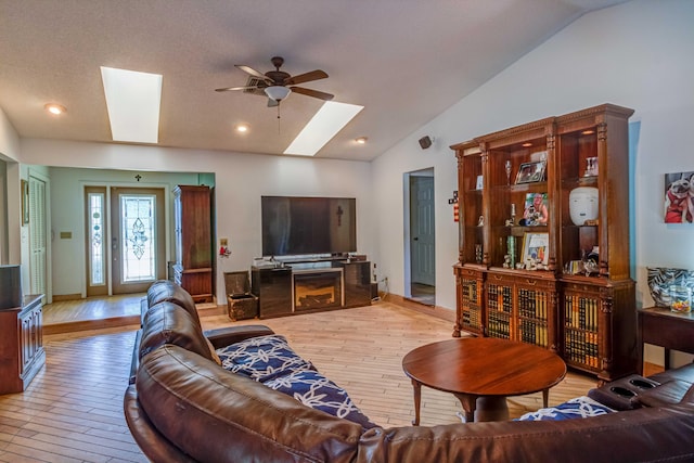 living room with ceiling fan, vaulted ceiling with skylight, and light hardwood / wood-style flooring