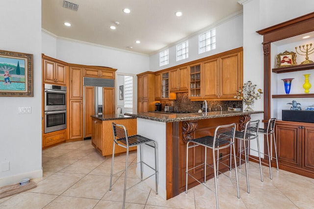 kitchen with a breakfast bar, dark stone counters, crown molding, double oven, and kitchen peninsula