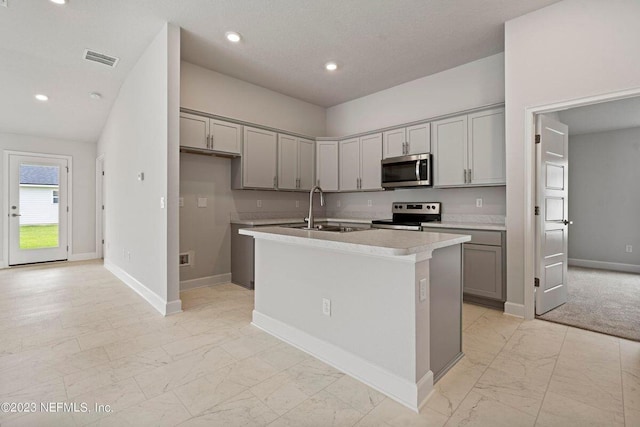 kitchen featuring gray cabinets, sink, an island with sink, and stainless steel appliances