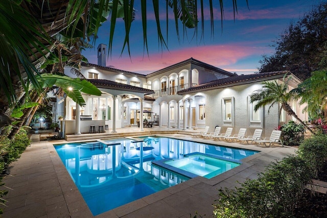 pool at dusk with a patio area, an in ground hot tub, and a bar