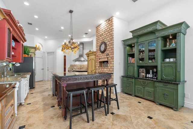 kitchen featuring an inviting chandelier, sink, a brick fireplace, wall chimney exhaust hood, and dark stone countertops