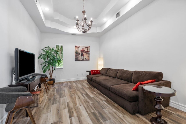 living room with hardwood / wood-style floors, a tray ceiling, and an inviting chandelier