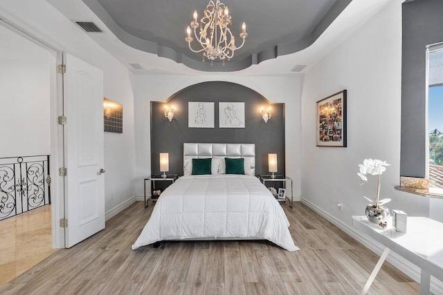 bedroom featuring light hardwood / wood-style floors, a raised ceiling, and an inviting chandelier