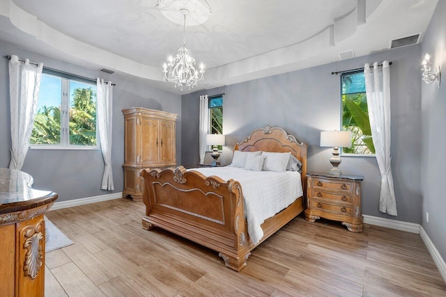 bedroom featuring a chandelier, a tray ceiling, and light hardwood / wood-style floors