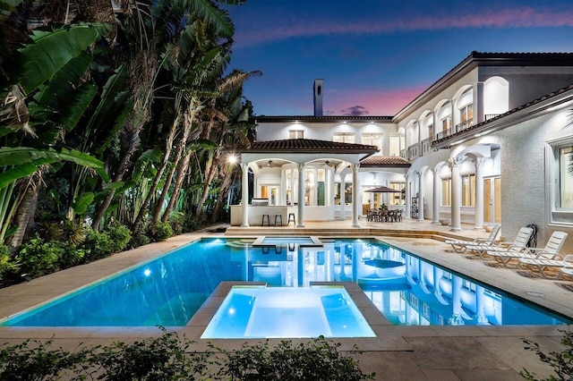 pool at dusk with an in ground hot tub and a patio