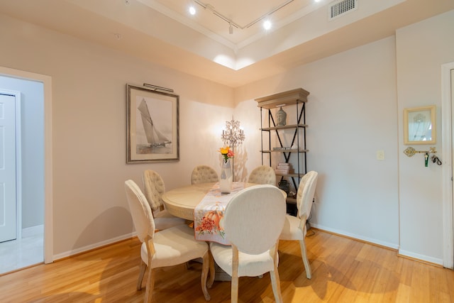 dining room featuring a raised ceiling, rail lighting, and light wood-type flooring