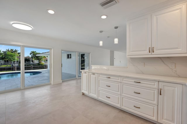 kitchen with backsplash, white cabinetry, light stone countertops, and pendant lighting