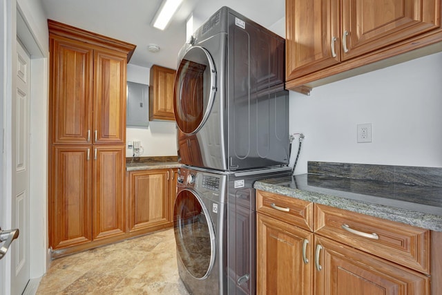 clothes washing area with cabinets, electric panel, and stacked washing maching and dryer