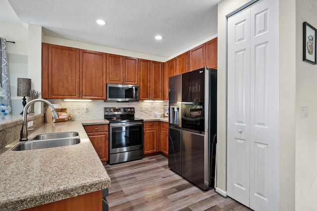 kitchen with light stone countertops, sink, backsplash, appliances with stainless steel finishes, and light wood-type flooring