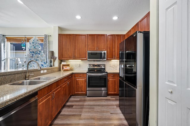 kitchen featuring decorative backsplash, light stone counters, stainless steel appliances, sink, and hardwood / wood-style floors