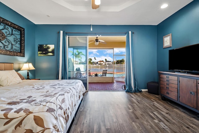 bedroom with ceiling fan, dark hardwood / wood-style floors, access to outside, and a tray ceiling