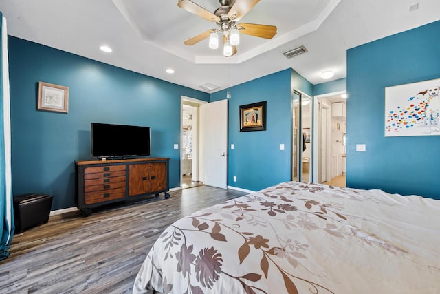 bedroom featuring hardwood / wood-style flooring, ceiling fan, a raised ceiling, and ensuite bath