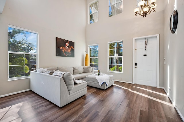 living room with dark hardwood / wood-style flooring, a towering ceiling, a healthy amount of sunlight, and a notable chandelier