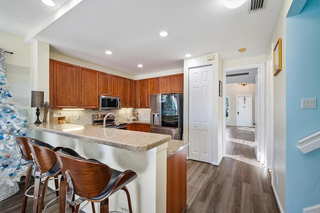 kitchen featuring stainless steel appliances, a kitchen breakfast bar, tasteful backsplash, dark hardwood / wood-style flooring, and kitchen peninsula