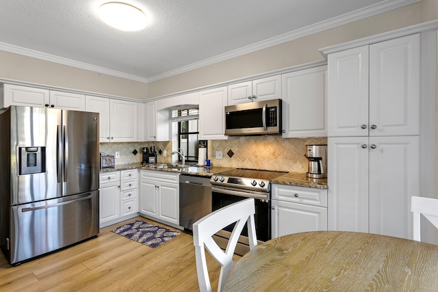 kitchen with white cabinetry, stainless steel appliances, ornamental molding, dark stone countertops, and light wood-type flooring