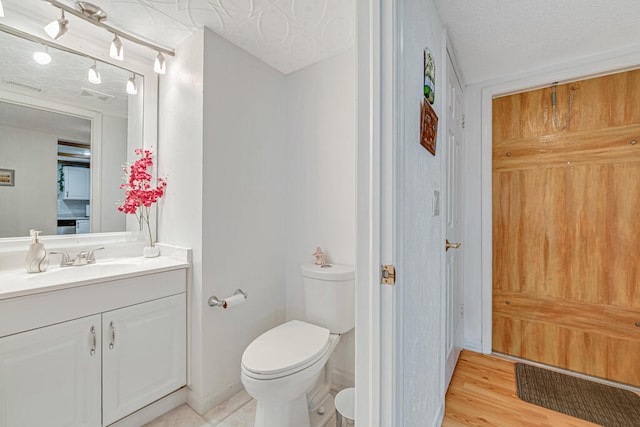 bathroom with wood-type flooring, vanity, a textured ceiling, and toilet