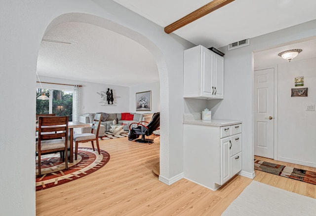 hallway with beamed ceiling, a textured ceiling, and light hardwood / wood-style flooring