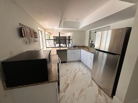 kitchen with kitchen peninsula, stainless steel appliances, sink, dark stone countertops, and white cabinets