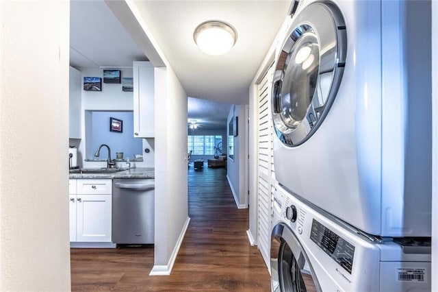 clothes washing area featuring stacked washer and dryer, laundry area, baseboards, dark wood finished floors, and a sink