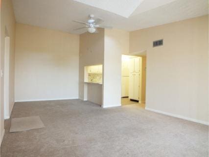 carpeted empty room featuring ceiling fan, a towering ceiling, and a skylight