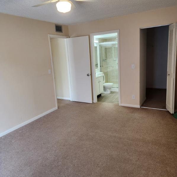 unfurnished bedroom with light carpet, ensuite bath, ceiling fan, a textured ceiling, and a closet