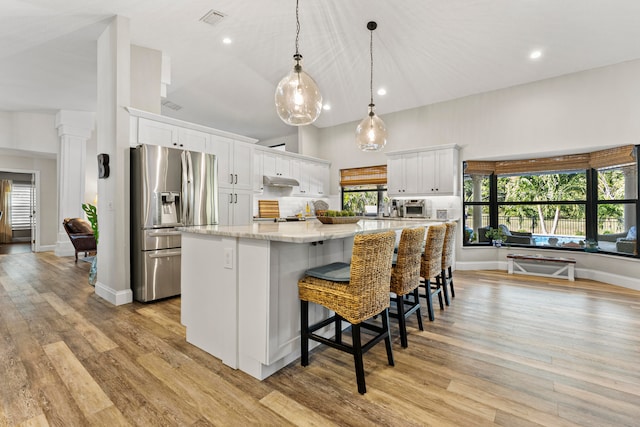 kitchen with a spacious island, hanging light fixtures, stainless steel fridge with ice dispenser, light stone counters, and white cabinetry