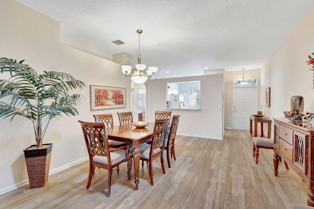 dining area featuring a textured ceiling, light hardwood / wood-style flooring, and a notable chandelier