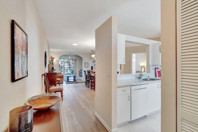 interior space with sink, light hardwood / wood-style flooring, white cabinetry, white dishwasher, and light stone counters