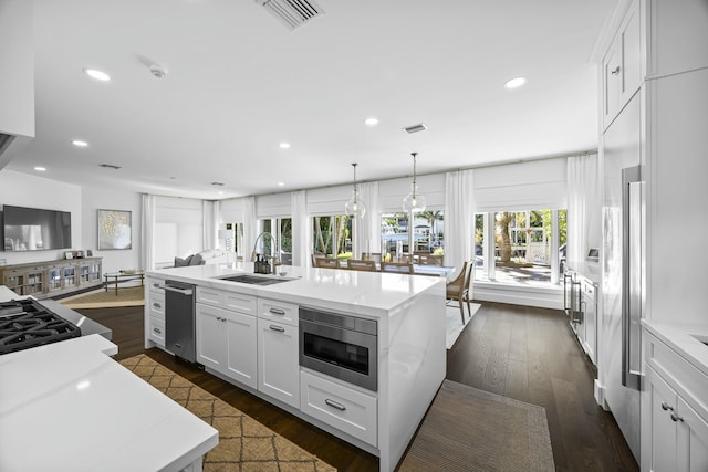 kitchen featuring white cabinets, stainless steel microwave, sink, and an island with sink