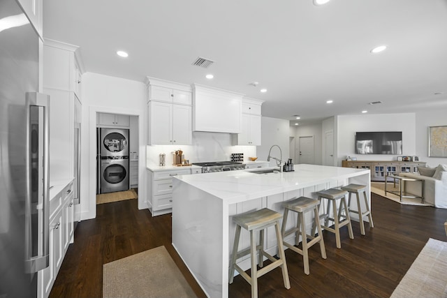 kitchen with dark hardwood / wood-style flooring, sink, a center island with sink, stacked washer and dryer, and white cabinetry