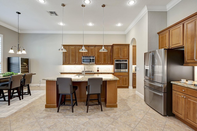 kitchen featuring a center island with sink, pendant lighting, light stone counters, and stainless steel appliances