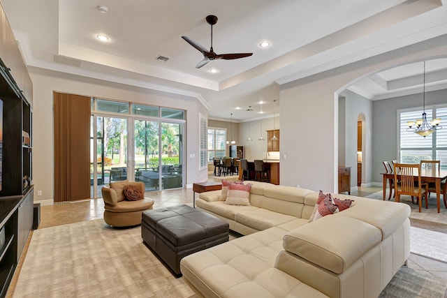 tiled living room featuring ceiling fan with notable chandelier, a raised ceiling, and crown molding