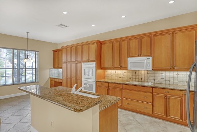 kitchen featuring light stone counters, white appliances, sink, hanging light fixtures, and an island with sink