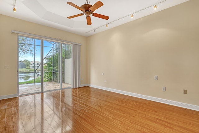 spare room featuring a water view, a raised ceiling, ceiling fan, and light hardwood / wood-style flooring