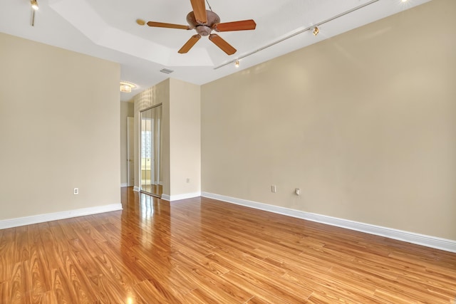 empty room with a tray ceiling, ceiling fan, and light hardwood / wood-style floors