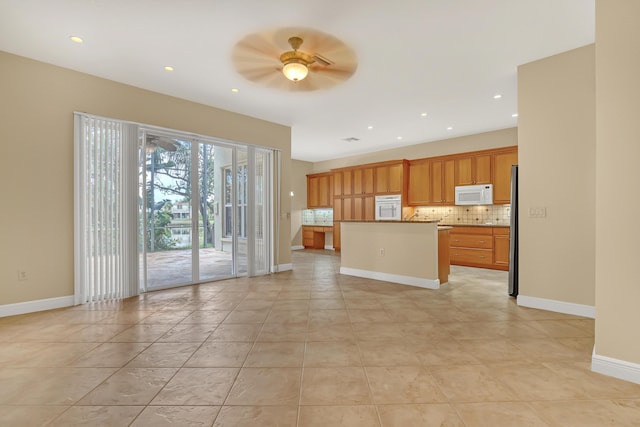 kitchen featuring a center island, backsplash, ceiling fan, light tile patterned flooring, and stainless steel refrigerator