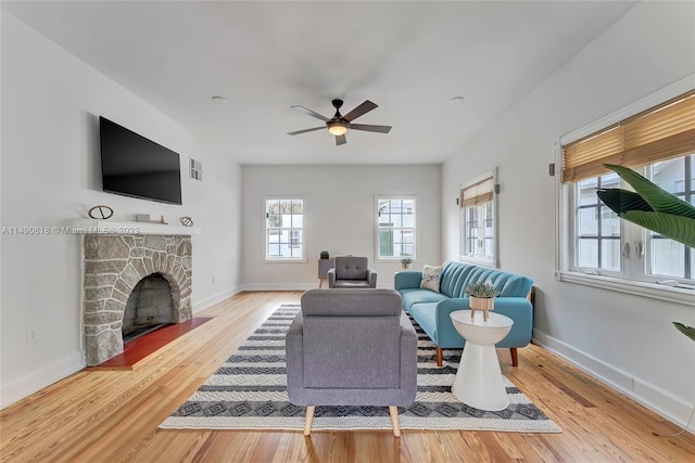 living room featuring hardwood / wood-style floors, ceiling fan, and a stone fireplace