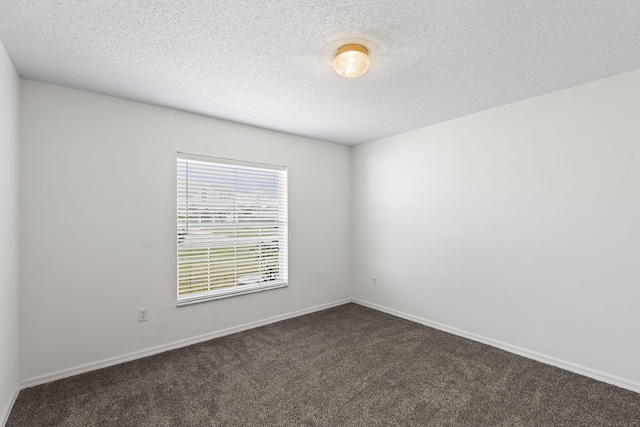 spare room with a textured ceiling and dark colored carpet