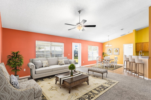 carpeted living room featuring a textured ceiling, ceiling fan with notable chandelier, a healthy amount of sunlight, and vaulted ceiling