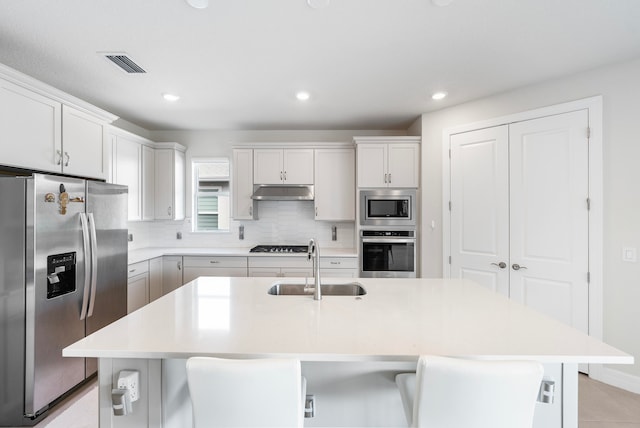 kitchen with a breakfast bar area, white cabinetry, an island with sink, and stainless steel appliances