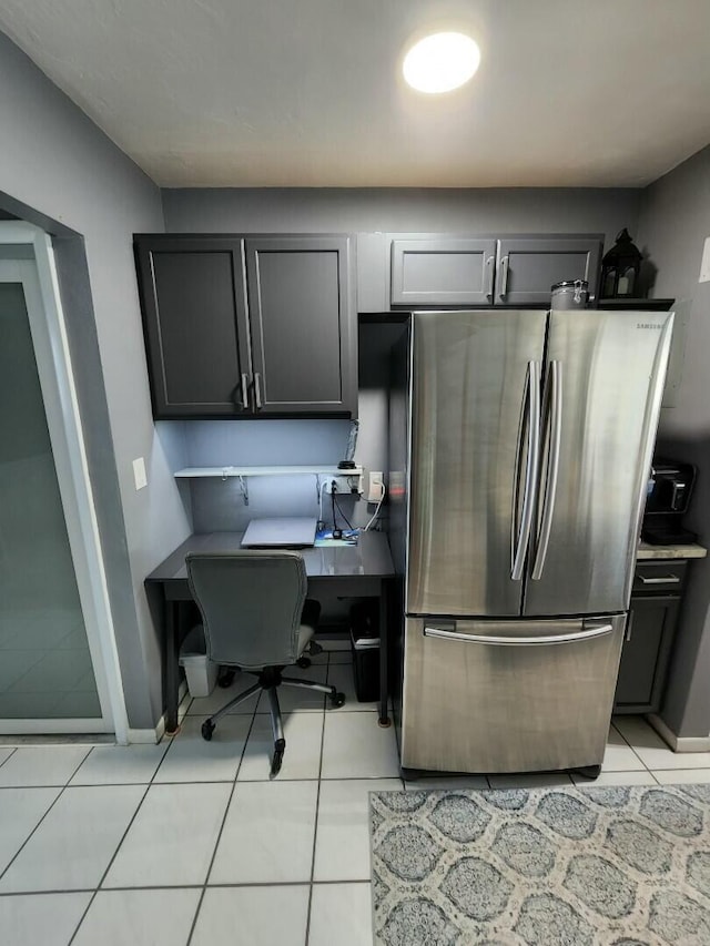 kitchen with light tile patterned floors, baseboards, freestanding refrigerator, and gray cabinetry