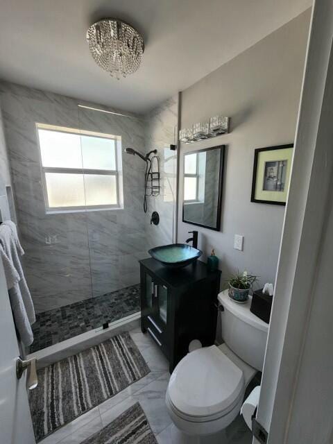 bathroom with a tile shower, a wealth of natural light, vanity, and toilet