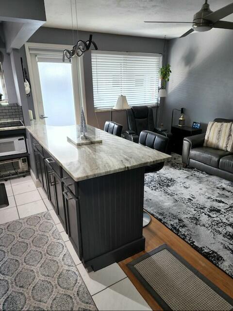 kitchen with a center island, ceiling fan, light tile patterned floors, tasteful backsplash, and pendant lighting