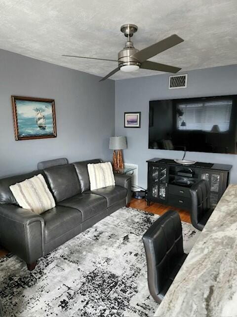 living room featuring ceiling fan, hardwood / wood-style floors, and a textured ceiling