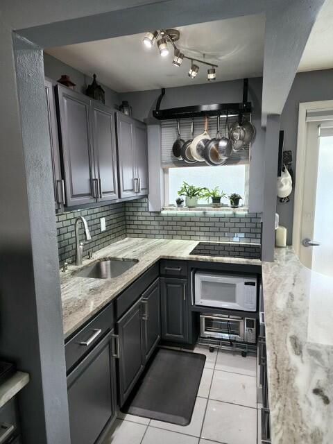 kitchen featuring sink, white microwave, light tile patterned floors, backsplash, and black electric stovetop