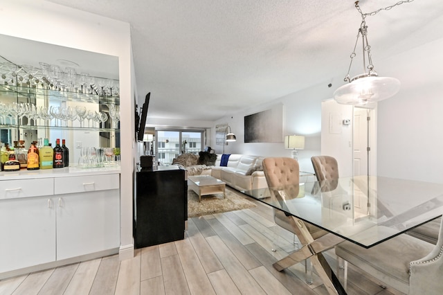 dining room with a textured ceiling, bar, and light hardwood / wood-style flooring